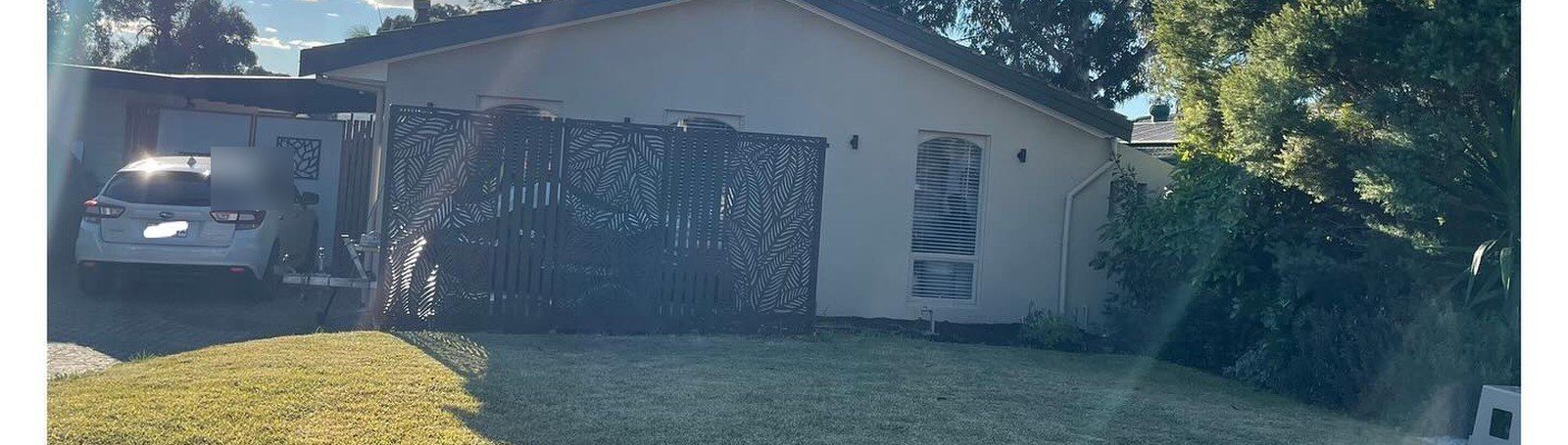 A pale, dry front lawn in front of a rendered house with a decorative screen
