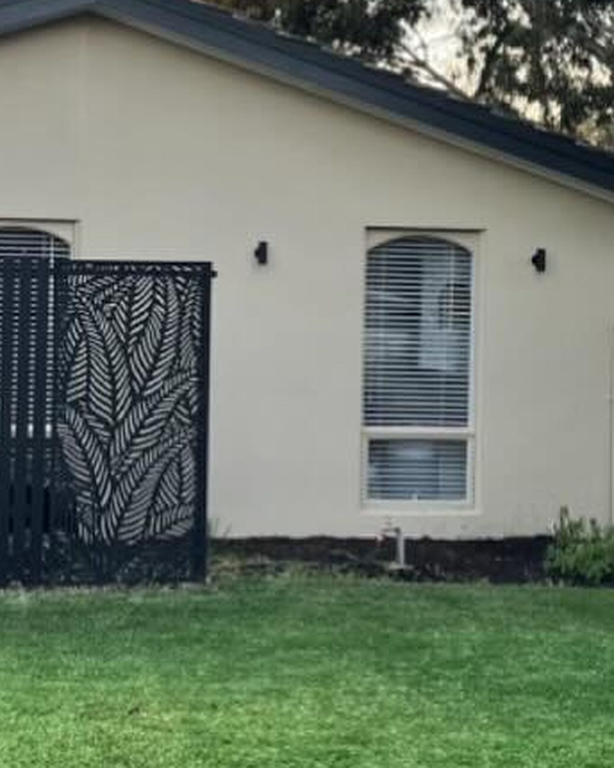 A vivid green painted lawn in front of a cream house with a black screen fence